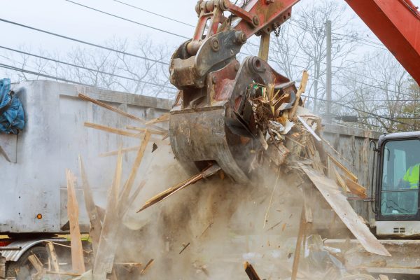 Truck with excavator loads construction waste on a dump truck disposal bin